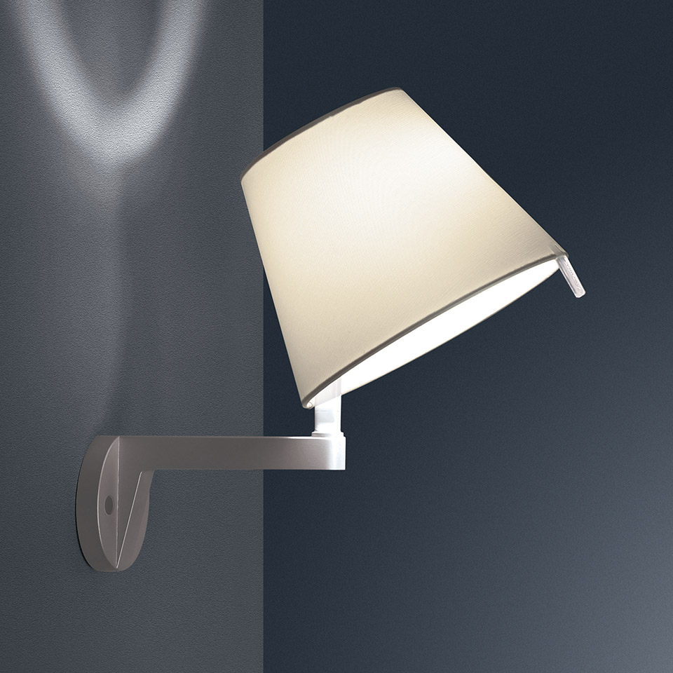 Lampada da parete Artemide Melampo Parete con paralume in tessuto avorio su staffa in alluminio, inclinata per dirigere la luce verso il basso su parete grigia