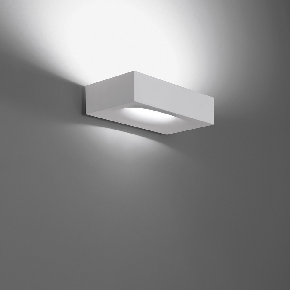 Applique da parete Artemide Melete, corpo rettangolare bianco, emette fasci di luce verso l'alto e il basso su parete grigia