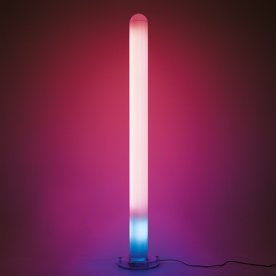 Lampada da terra Artemide Metacolor: alto diffusore cilindrico con luce sfumata dal rosa-bianco in alto al ciano-blu alla base, su supporto rotondo trasparente