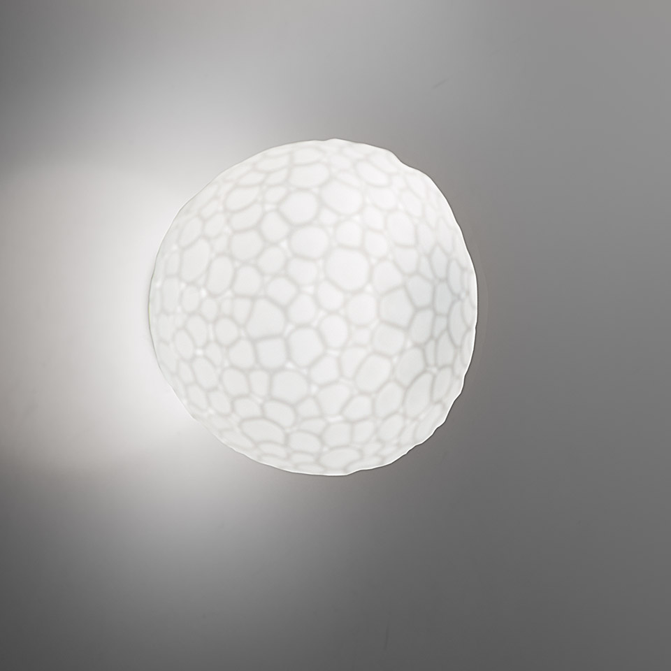 Lampada da parete/soffitto Artemide Meteorite: diffusore sferico bianco con texture organica a celle, emette luce soffusa