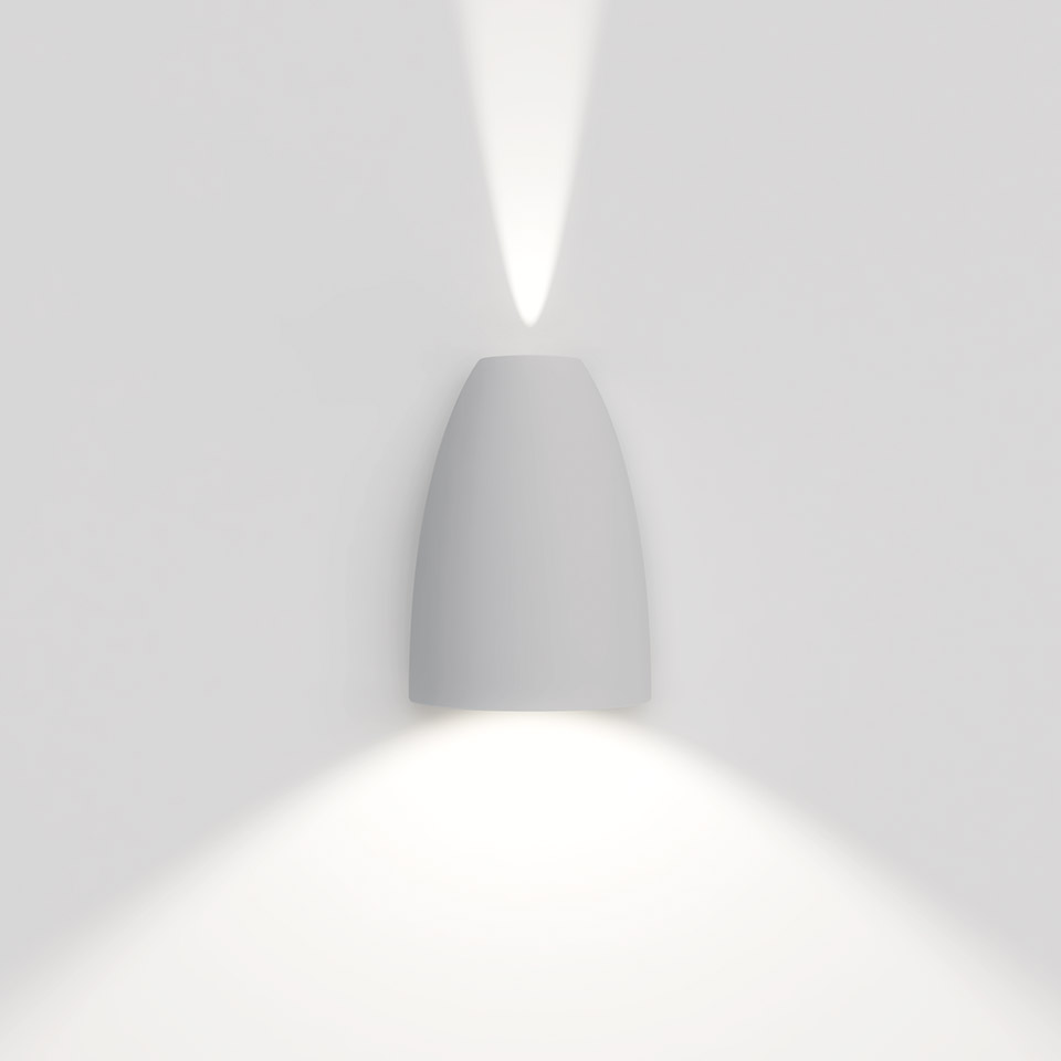 Applique Artemide Molla bianca a forma di proiettile che emette fasci di luce verso l'alto e il basso su parete bianca