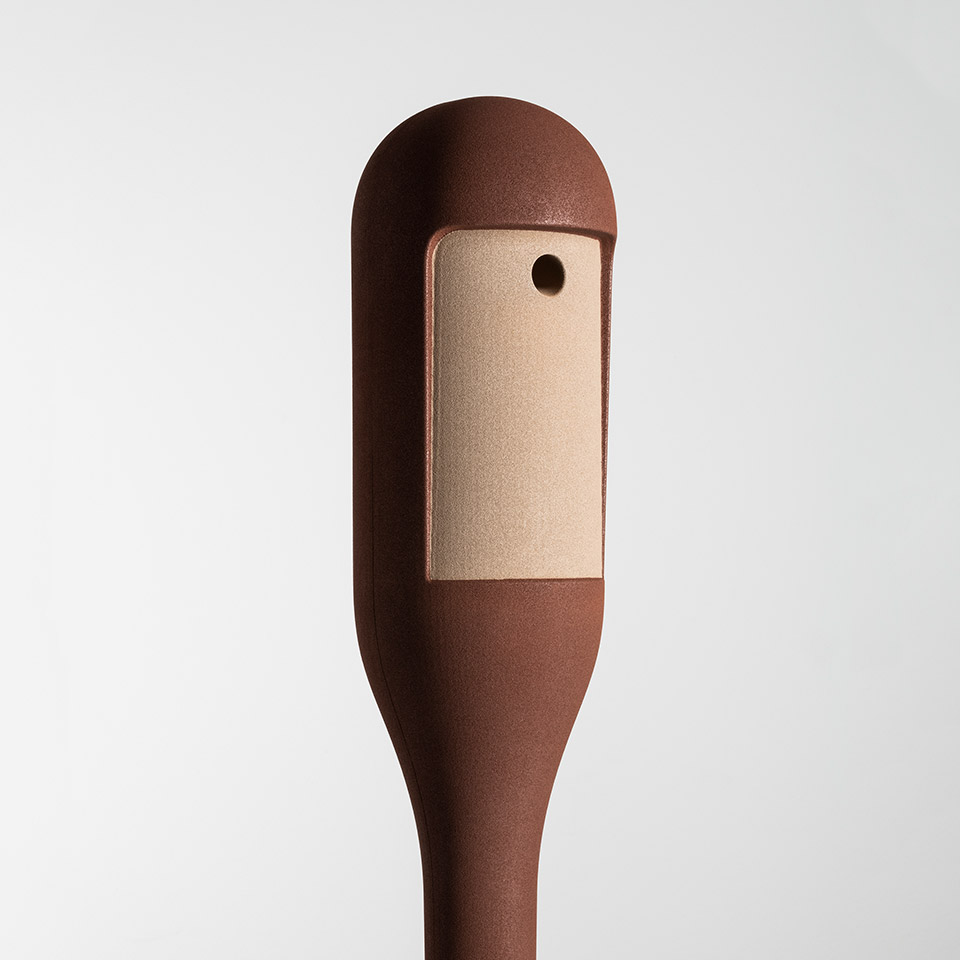 Dettaglio testa lampada Artemide Needoo: corpo arrotondato marrone scuro con pannello LED rettangolare color rame e piccolo pulsante di controllo