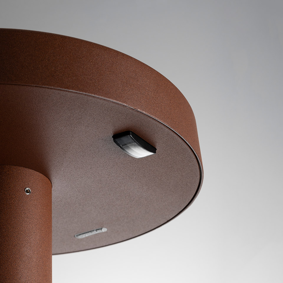 Primo piano della base della lampada da esterno Artemide Needoo in finitura marrone ruggine, con sensore di movimento e porta di ricarica sul fondo