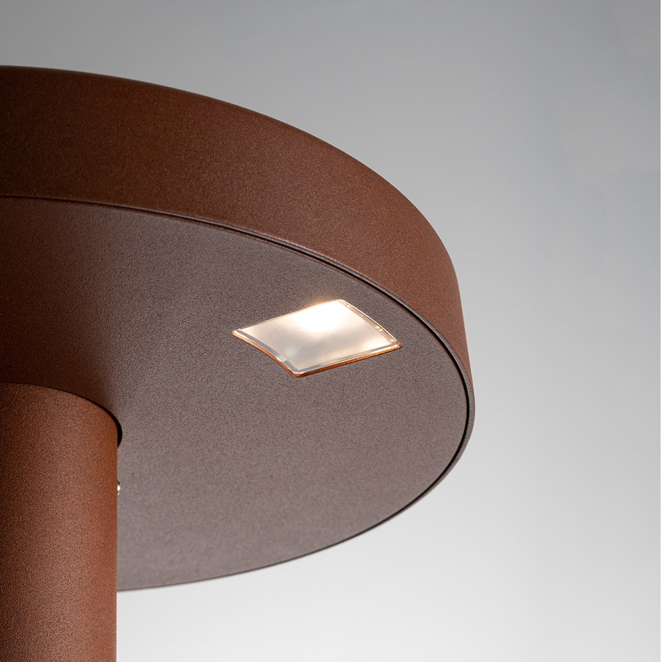 Primo piano del paletto da esterno Artemide Needoo in finitura marrone ruggine, con lente LED quadrata opaca sul cappello circolare superiore