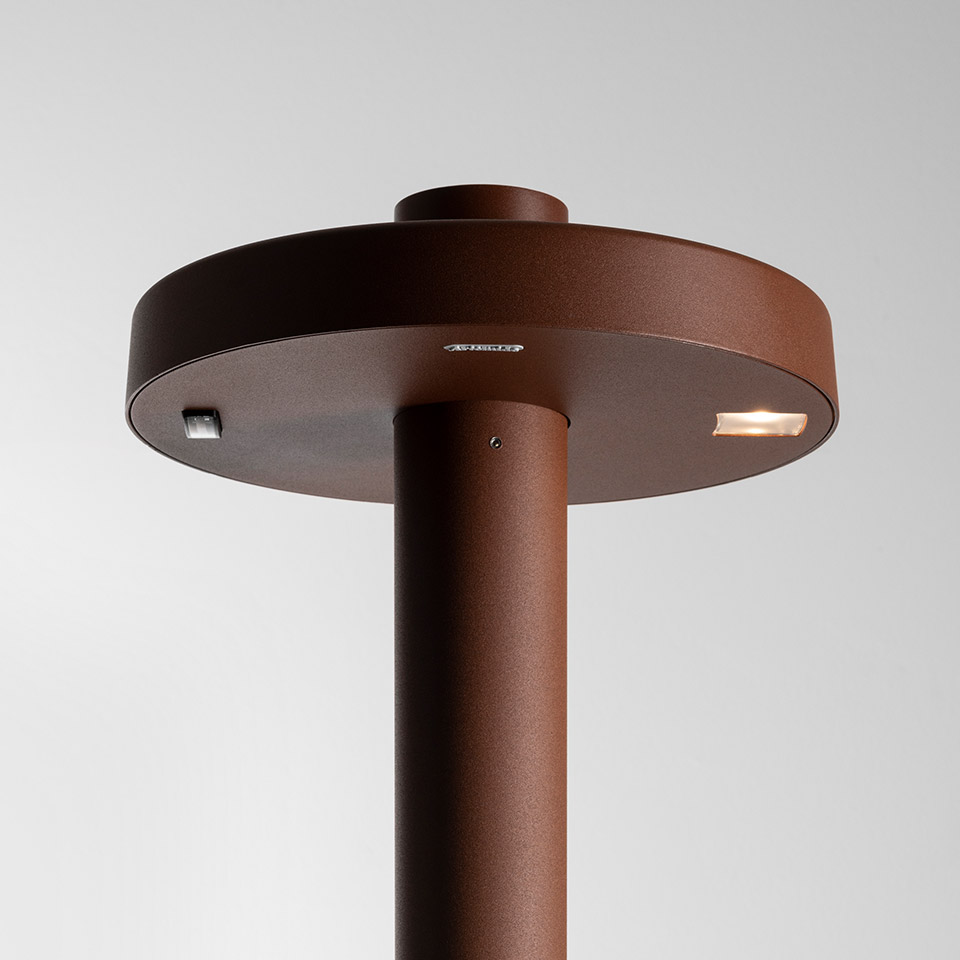 Lampada da terra per esterni Artemide Needoo, primo piano del fusto cilindrico marrone ruggine con testa a disco circolare e luce LED integrata