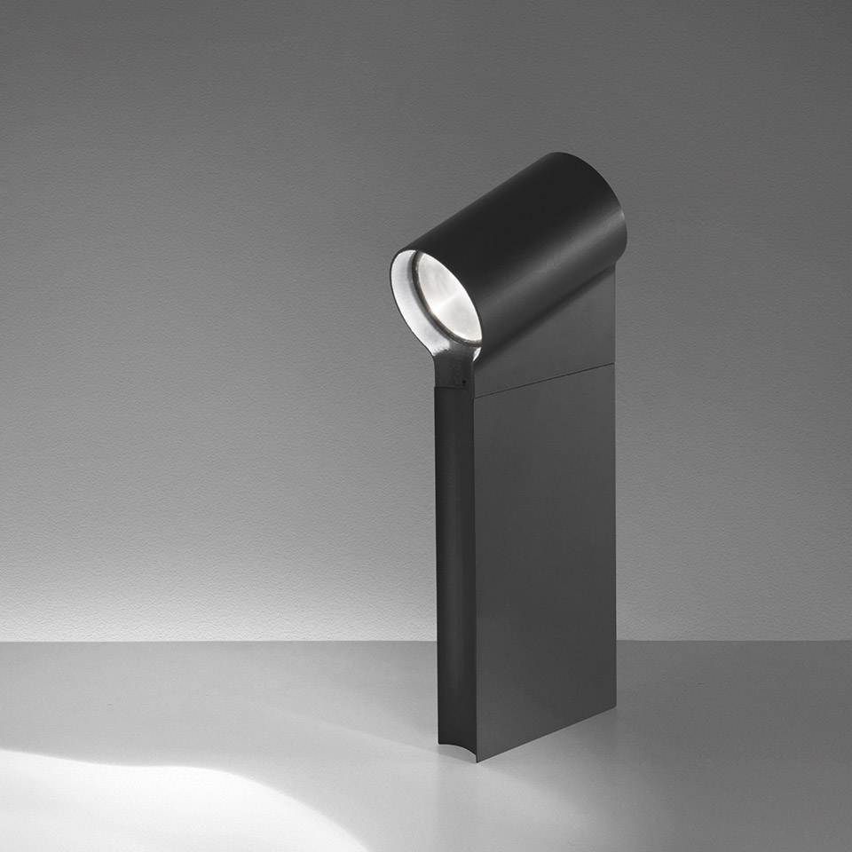 Paletto luminoso da esterno Artemide Oblique in grigio scuro, con testa cilindrica LED orientabile che proietta luce direzionale verso il basso