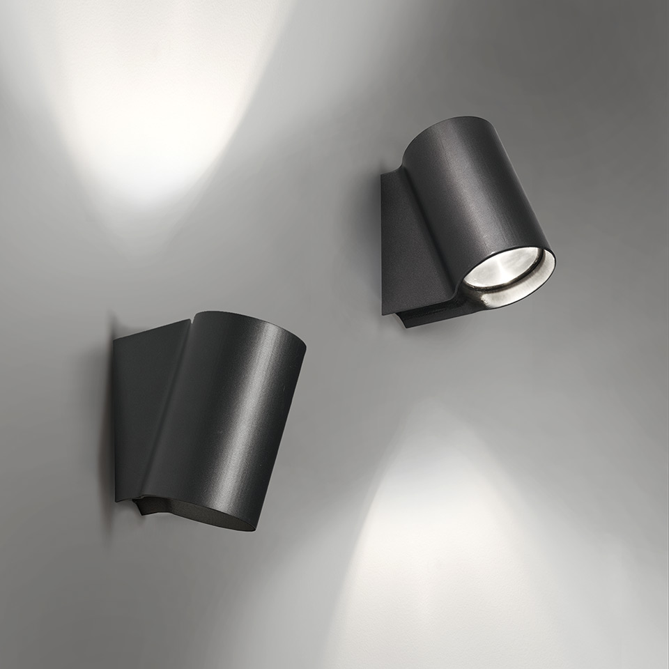 Due faretti da parete Artemide Oblique grigio scuro: sinistro inclinato verso l'alto con luce diffusa, destro orientato verso il basso con fascio concentrato