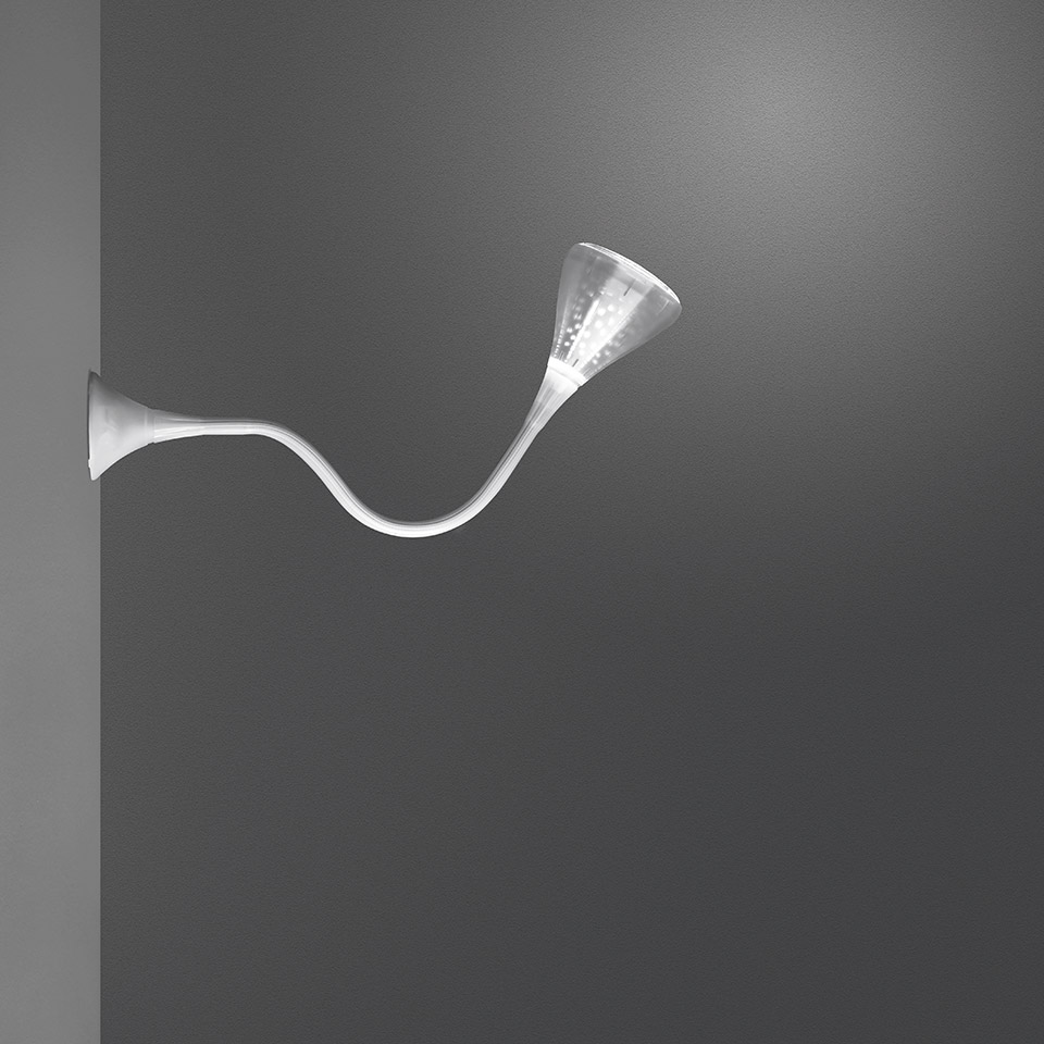 Lampada da parete Artemide Pipe: braccio bianco sinuoso che si estende dalla parete, terminante in un diffusore conico rivolto verso l'alto che emette luce soffusa