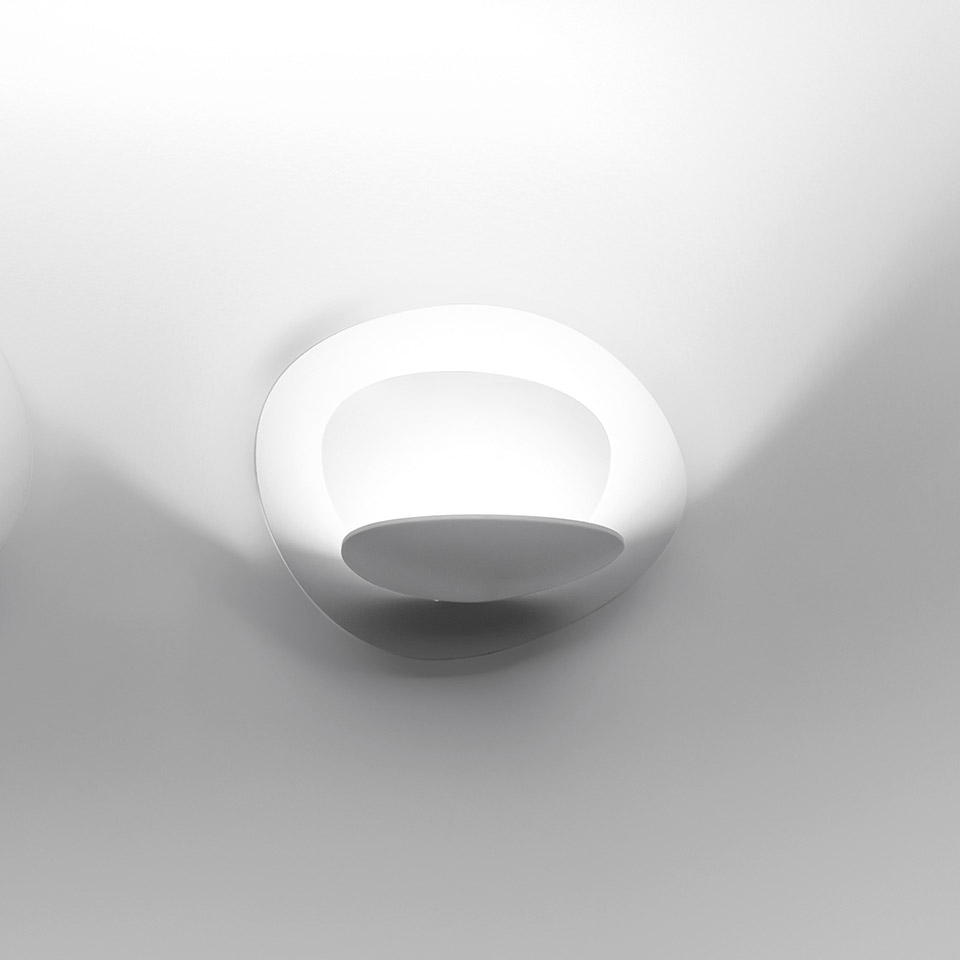 Artemide Pirce Parete wall lamp: white oval sculptural diffuser emitting soft upward and downward light against a white wall