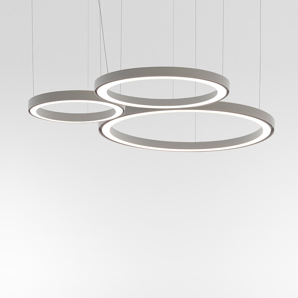 Tre lampade a sospensione Artemide Ripple: anelli LED circolari grigi, sospesi a diverse altezze, nelle dimensioni piccola, media e grande