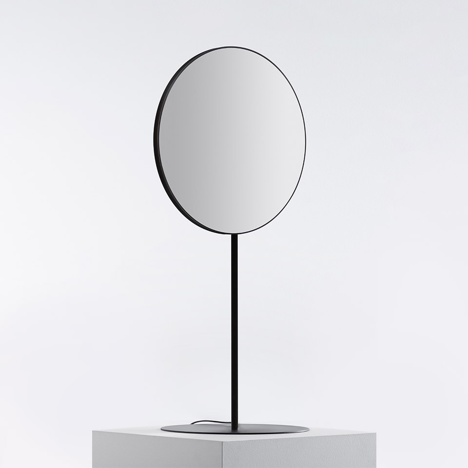 Specchio da tavolo Artemide Se|eS con superficie circolare riflettente, sottile cornice in metallo nero e stelo esile su base rotonda