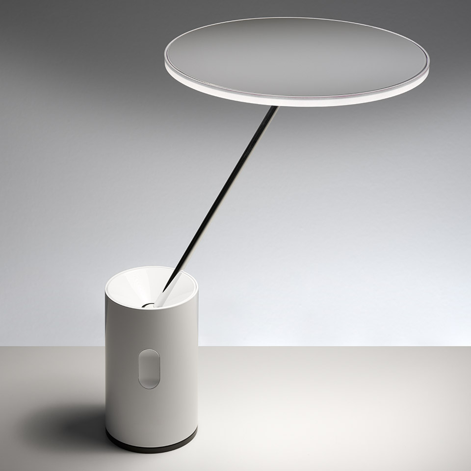 Artemide Sisifo table lamp: white cylindrical base with angled slim stem supporting a large flat circular LED diffuser