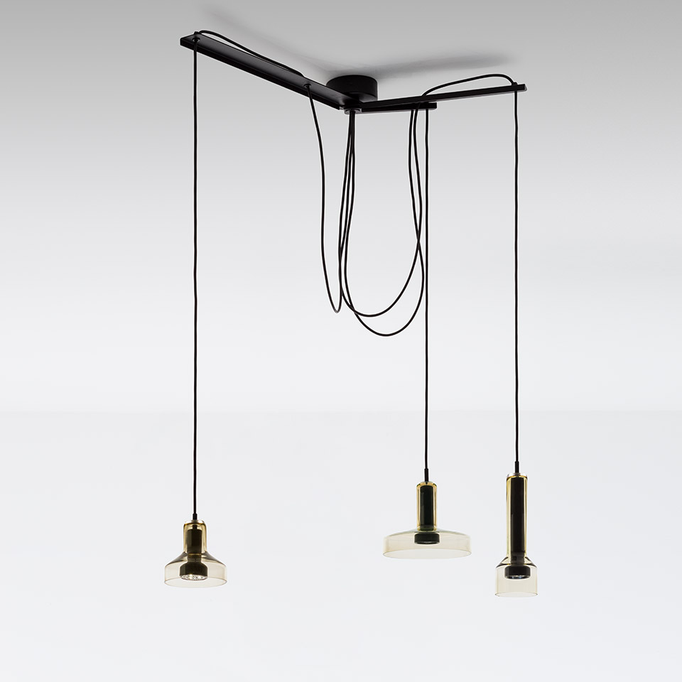 Artemide Stablight: tre lampade a sospensione con diffusori in vetro ambrato e finiture in ottone, sospese a diverse altezze da una rosone nero a soffitto con cavi neri ad anello
