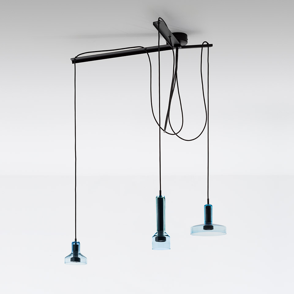 Artemide Stablight: tre lampade a sospensione con diffusori in vetro azzurrato appesi a diverse altezze da una barra nera a soffitto su cavi neri