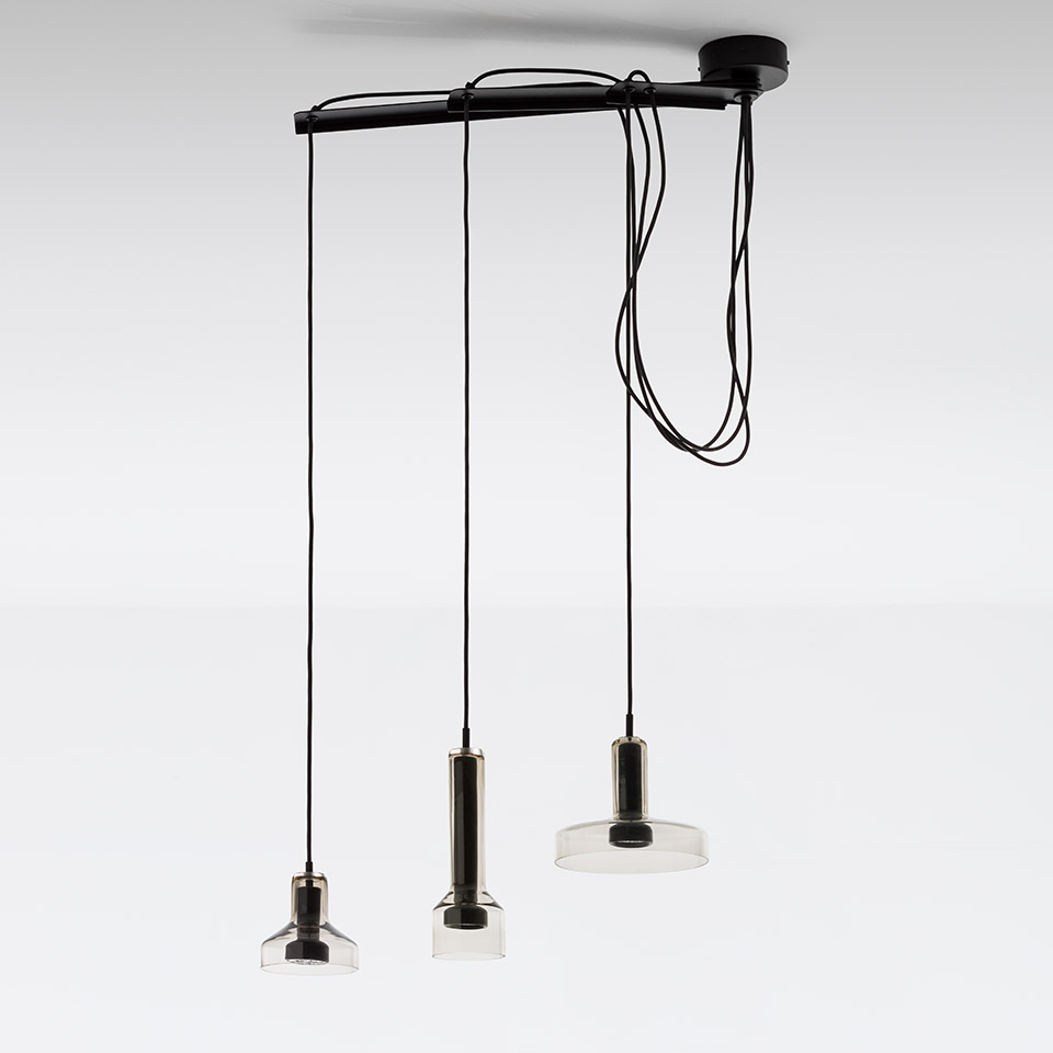 Artemide Stablight: tre lampade a sospensione su barra nera, altezze diverse, corpi cilindrici in metallo con diffusori in vetro trasparente, cavi neri