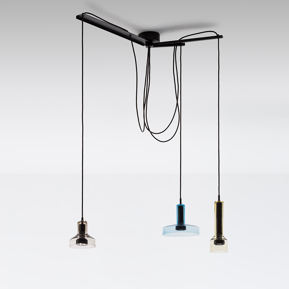 Artemide Stablight: tre lampade a sospensione su cavi neri da barra a soffitto, con paralumi cilindrici in vetro fumé, blu e ambra