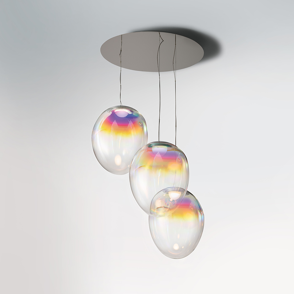 Sospensione Artemide Stellar Nebula: tre globi ovali in vetro iridescente con riflessi arcobaleno, sospesi a diverse altezze da un rosone rotondo