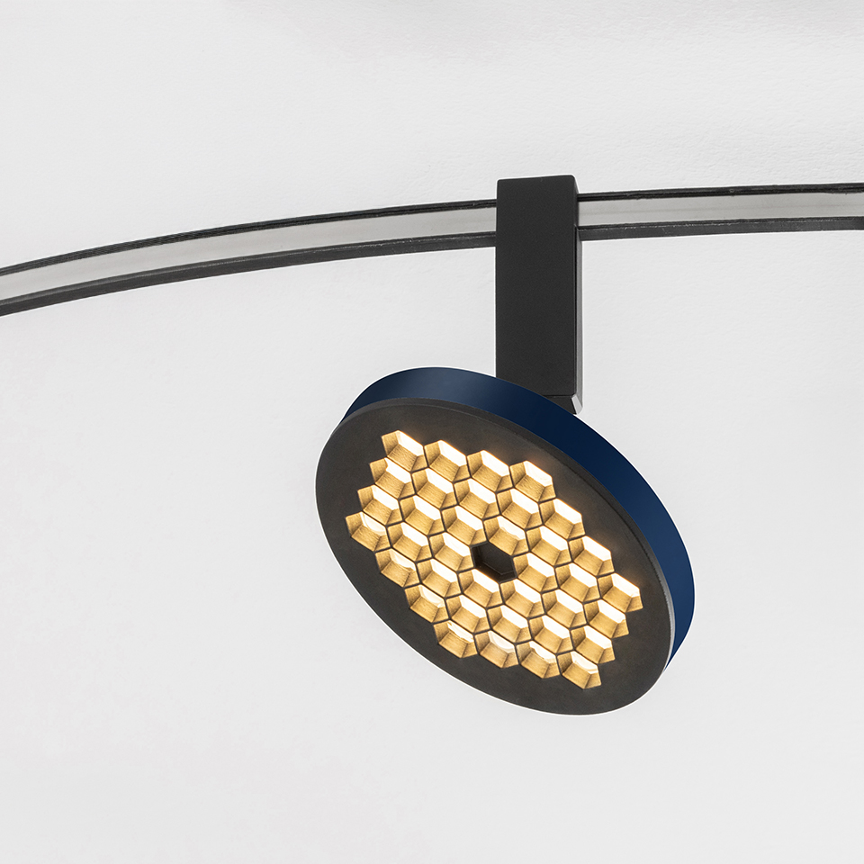 Faretto su binario Artemide Sylt con testa circolare blu e nera con griglia LED a nido d'ape, montato su binario curvo nero