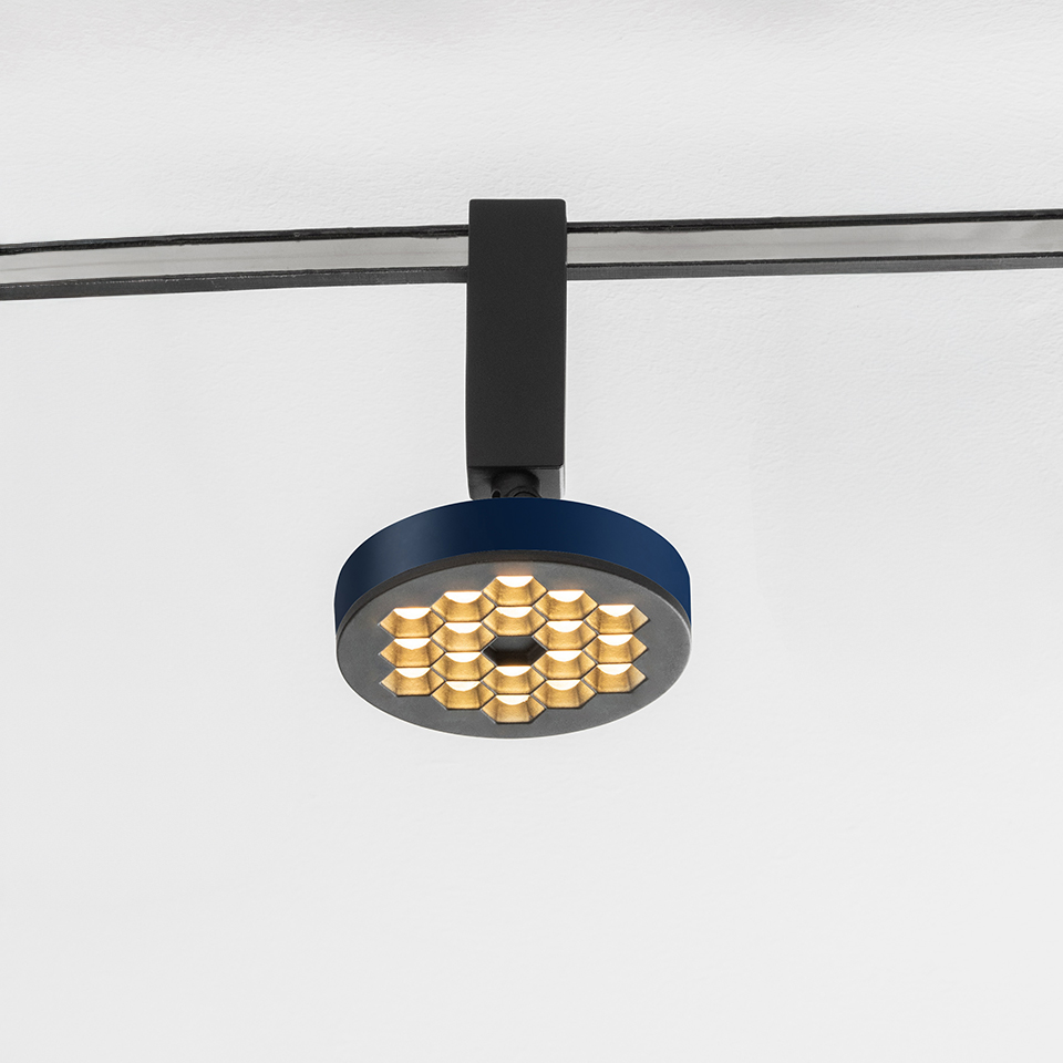 Faretto su binario Artemide Sylt con corpo circolare blu, griglia LED dorata a nido d'ape, montato su sistema a binario nero