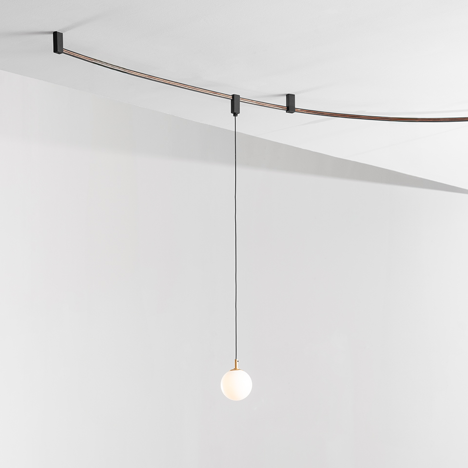 Lampada a sospensione Artemide Sylt: sfera in vetro opalino con dettaglio in ottone appesa a un cavo nero su sistema a cavo curvo a soffitto