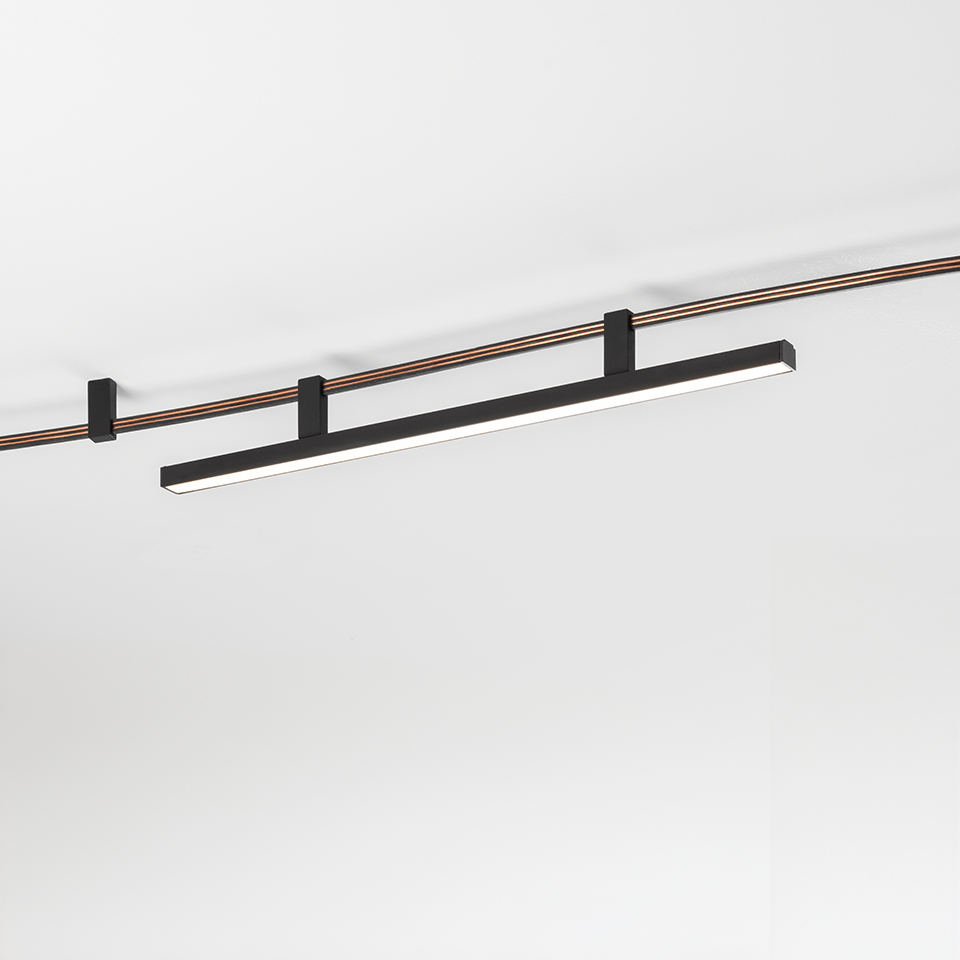 Luce da binario LED lineare Artemide Sylt in nero opaco, montata su sistema a doppio binario da soffitto in rame e nero
