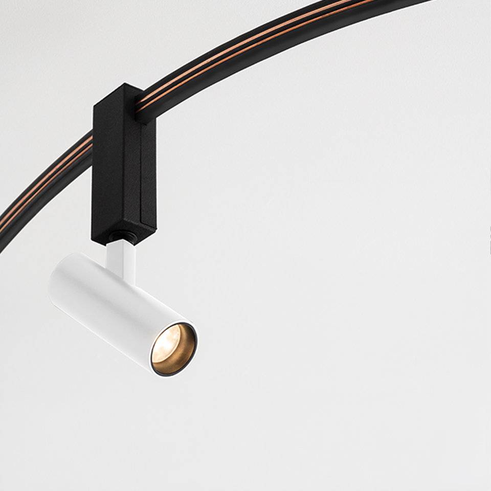 Faretto su binario Artemide Sylt: testa cilindrica LED bianca su adattatore rettangolare nero montato su binario curvo nero con cablaggio arancione