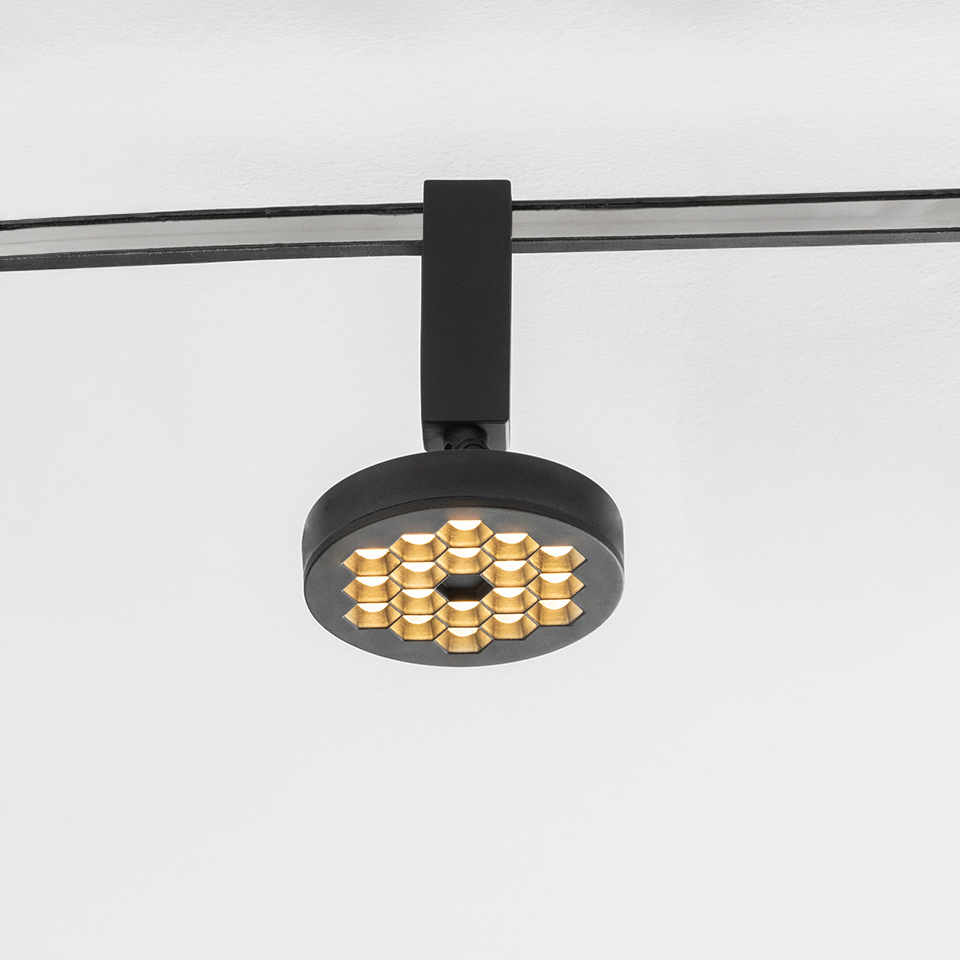 Faretto su binario Artemide Sylt nero con testa circolare a griglia LED a nido d'ape dorata, montato su binario a soffitto