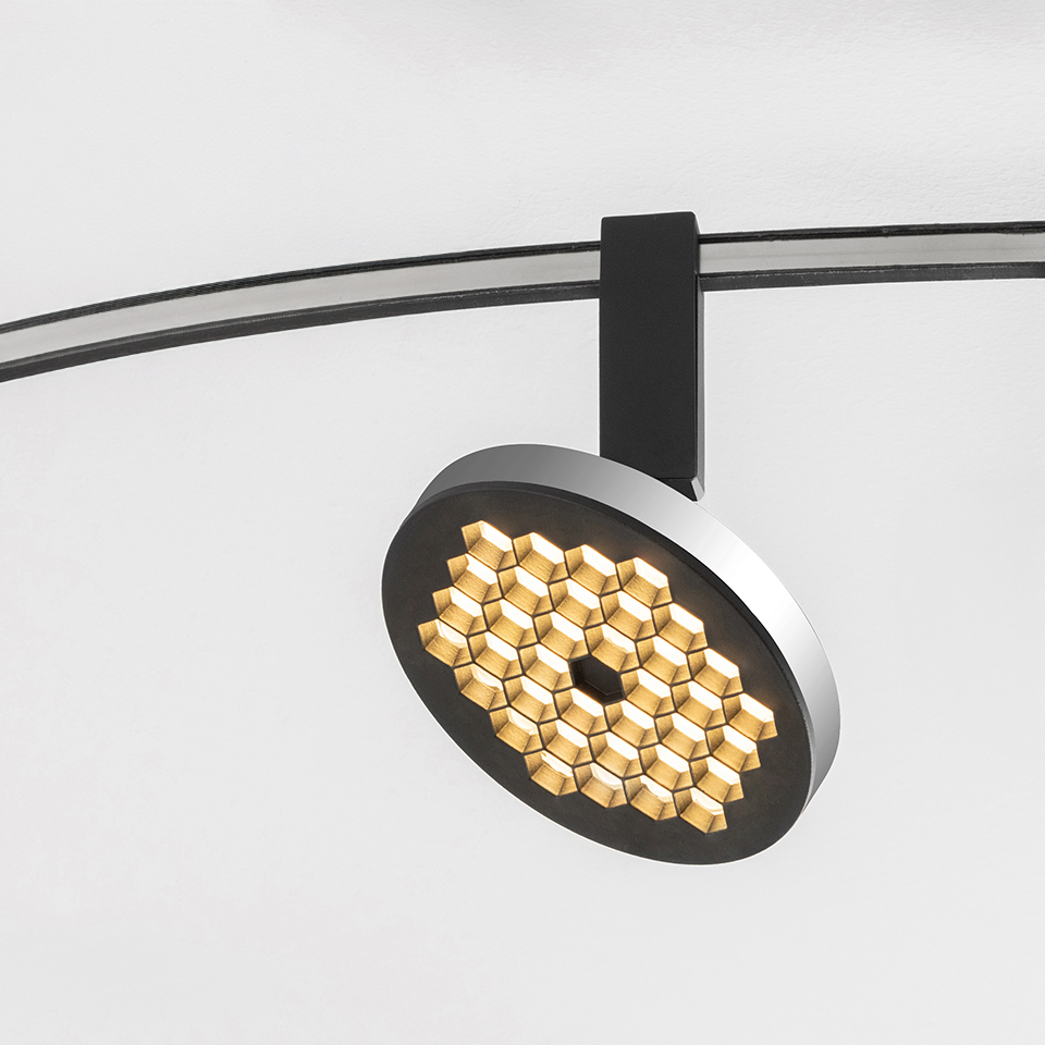 Faretto su binario Artemide Sylt con testa circolare a griglia LED a nido d'ape dorata, montato su binario curvo nero