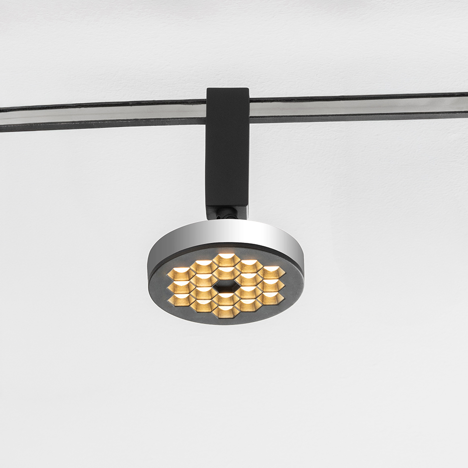 Faretto su binario Artemide Sylt con corpo circolare argento, matrice LED dorata a nido d'ape, montato su sistema a binario nero