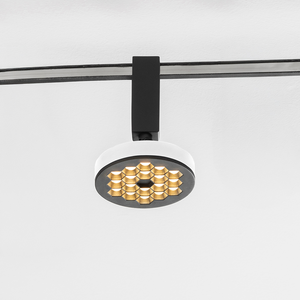 Faretto su binario Artemide Sylt con corpo rotondo bianco, griglia antiriflesso a nido d'ape nera e array LED dorato, montato su binario nero