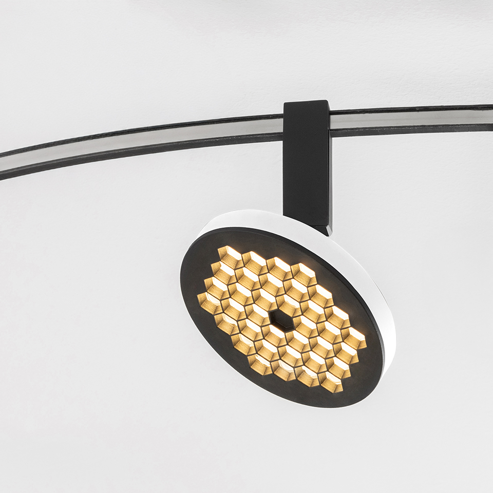 Faretto su binario Artemide Sylt con testa circolare bianca e nera con griglia LED a nido d'ape dorata, montato su binario curvo nero