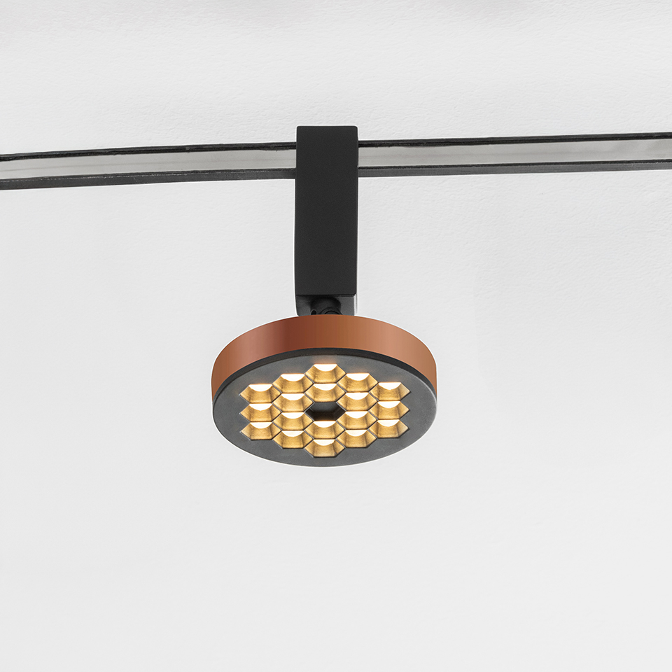 Faretto su binario Artemide Sylt con corpo circolare color rame, griglia LED a nido d'ape dorata, montato su sistema a binario nero