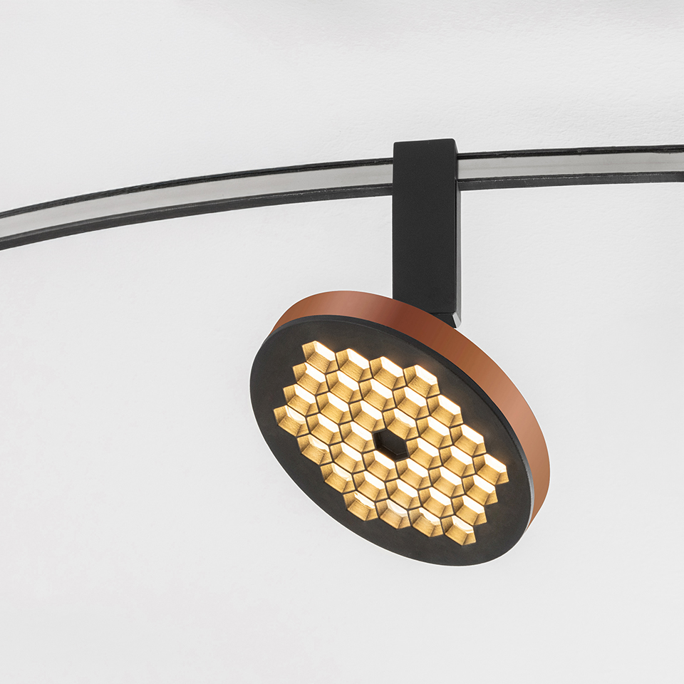 Faretto su binario Artemide Sylt con testa circolare nera e rame con griglia LED a nido d'ape, montato su binario curvo nero