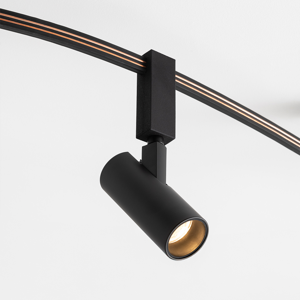 Faretto su binario Artemide Sylt nero opaco, testa cilindrica con interno dorato, montato su sistema a binario curvo nero
