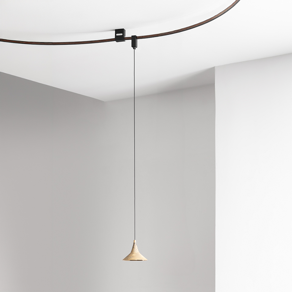 Lampada a sospensione Artemide Sylt con piccolo paralume conico beige appeso a un cavo sottile su binario curvo scuro a soffitto