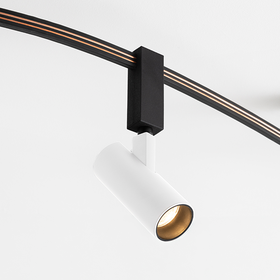 Faretto su binario Artemide Sylt: testa cilindrica bianca con interno dorato, montata su sistema a binario nero curvo tramite adattatore nero
