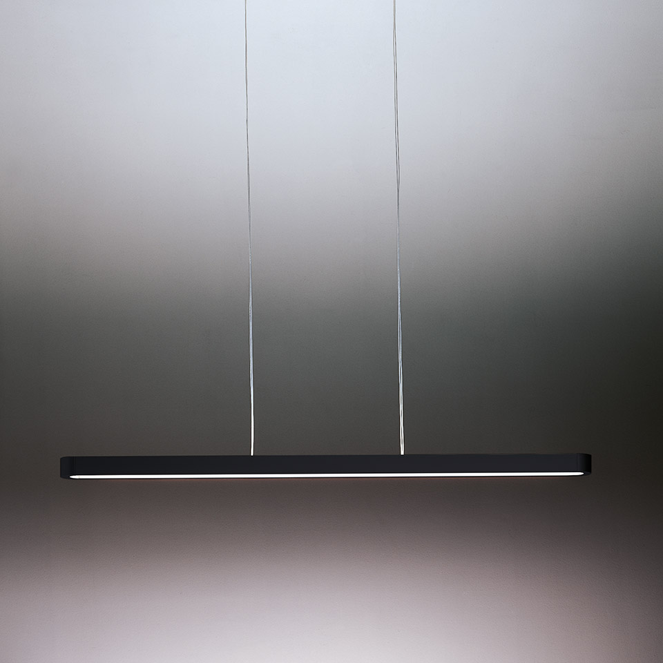 Lampada a sospensione Talo di Artemide: sottile barra LED lineare scura appesa a due cavi sottili, emette luce diffusa calda.