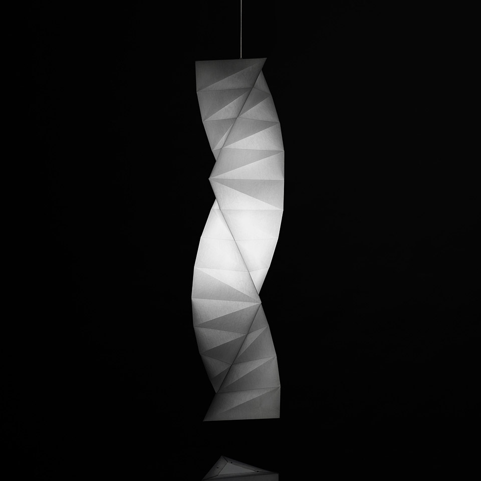 Lampada a sospensione Artemide In-Ei Issey Miyake Tatsuno-Otoshigo: diffusore bianco a spirale ispirato all'origami che emette luce soffusa su sfondo scuro