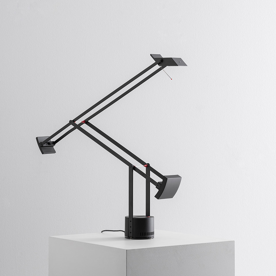 Lampada da tavolo Artemide Tizio nera con doppio braccio articolato, sistema di bilanciamento a contrappeso e base circolare su superficie bianca