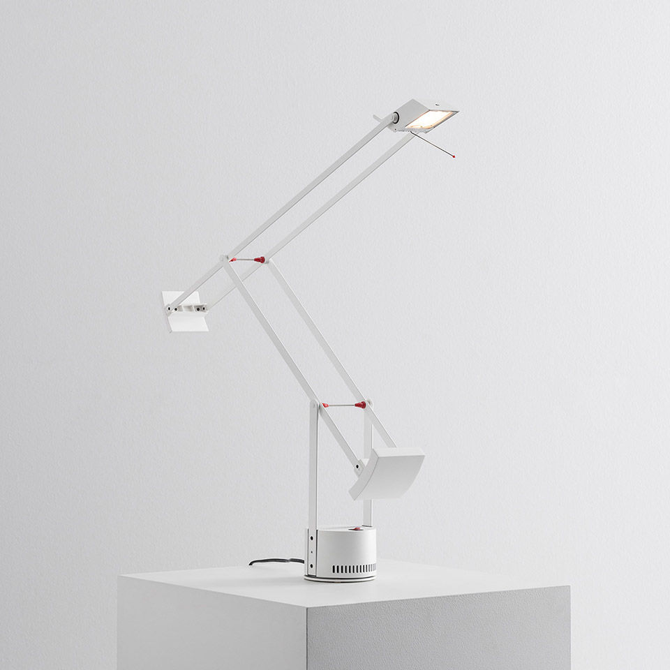 Lampada da tavolo Artemide Tizio bianca con bracci articolati, giunti rossi, testa orientabile e base circolare su superficie bianca