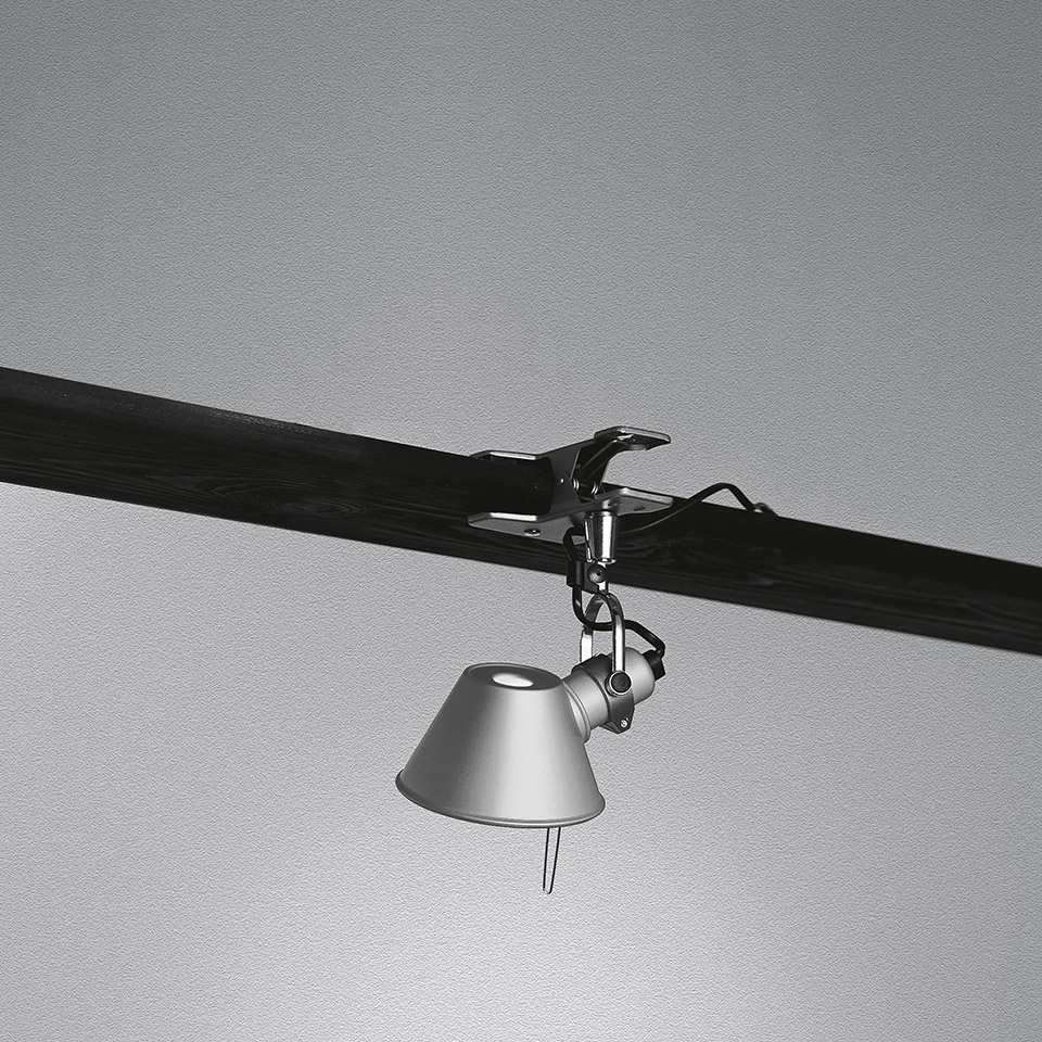 Lampada a pinza Artemide Tolomeo Pinza in alluminio, agganciata a una trave scura, con paralume conico orientabile rivolto verso il basso