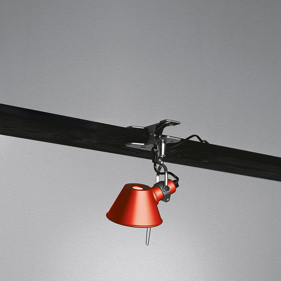Lampada a morsetto Artemide Tolomeo Pinza con paralume conico rosso, montata su binario orizzontale scuro tramite morsetto metallico regolabile