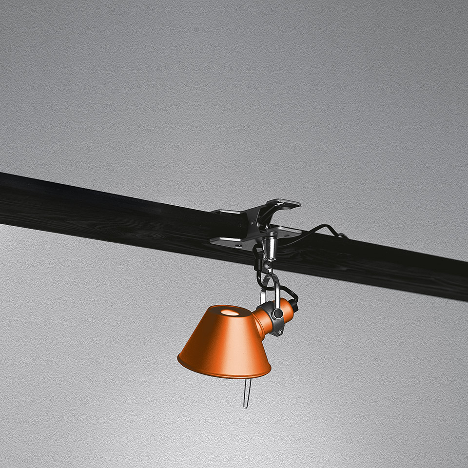 Lampada a morsetto Artemide Tolomeo Pinza arancione, fissata a una trave scura, con snodo regolabile e paralume conico rivolto verso il basso