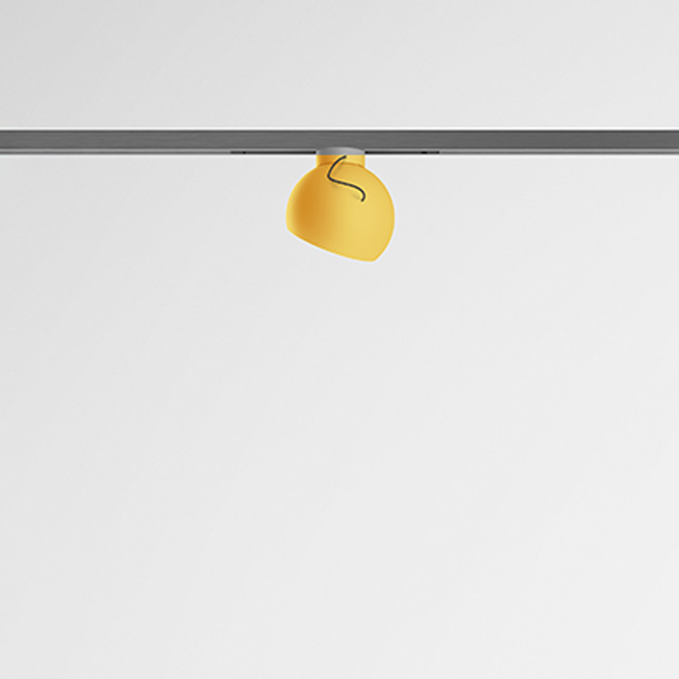 Artemide Turn Around System: faretto arrotondato giallo su binario grigio, con orientamento regolabile per illuminazione direzionale