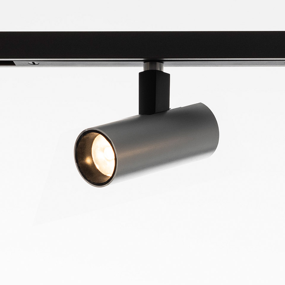 Artemide Turn Around System: faretto cilindrico in metallo scuro su binario nero, con emissione di luce bianca calda