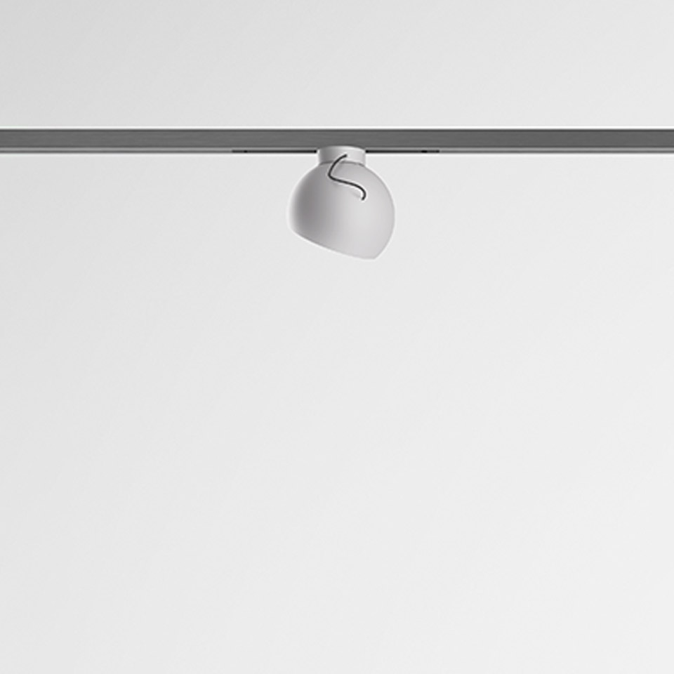 Artemide Turn Around System: faretto tondo bianco montato su binario a soffitto grigio, con testa orientabile