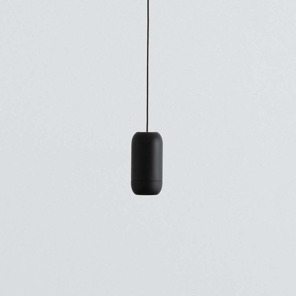 Lampada a sospensione Artemide Turn Around, corpo a capsula nero opaco appeso a un cavo nero su sfondo grigio chiaro