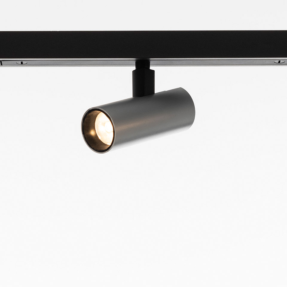 Artemide Turn Around System: faretto LED cilindrico bronzo scuro montato su binario nero, inclinato ad angolo
