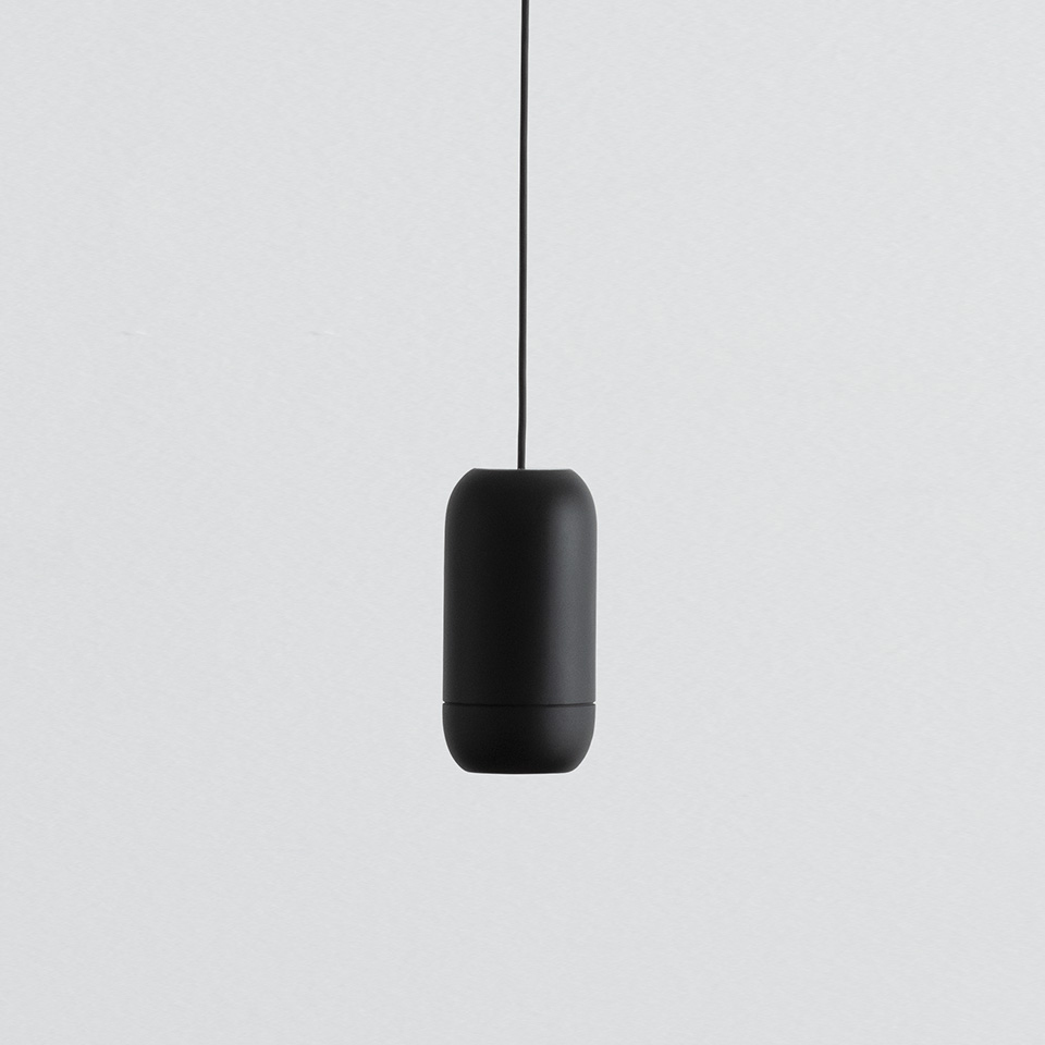 Lampada a sospensione Artemide Turn Around, corpo a capsula nero opaco sospeso da un cavo nero su sfondo grigio chiaro