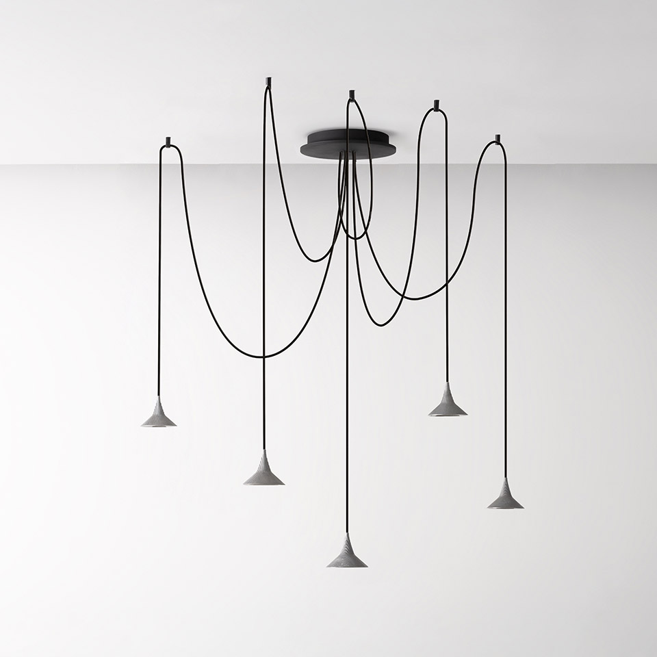 Lampadario multiplo Artemide Unterlinden: cinque paralumi conici in cemento su lunghi cavi neri drappeggiati da un'unica rosetta a soffitto